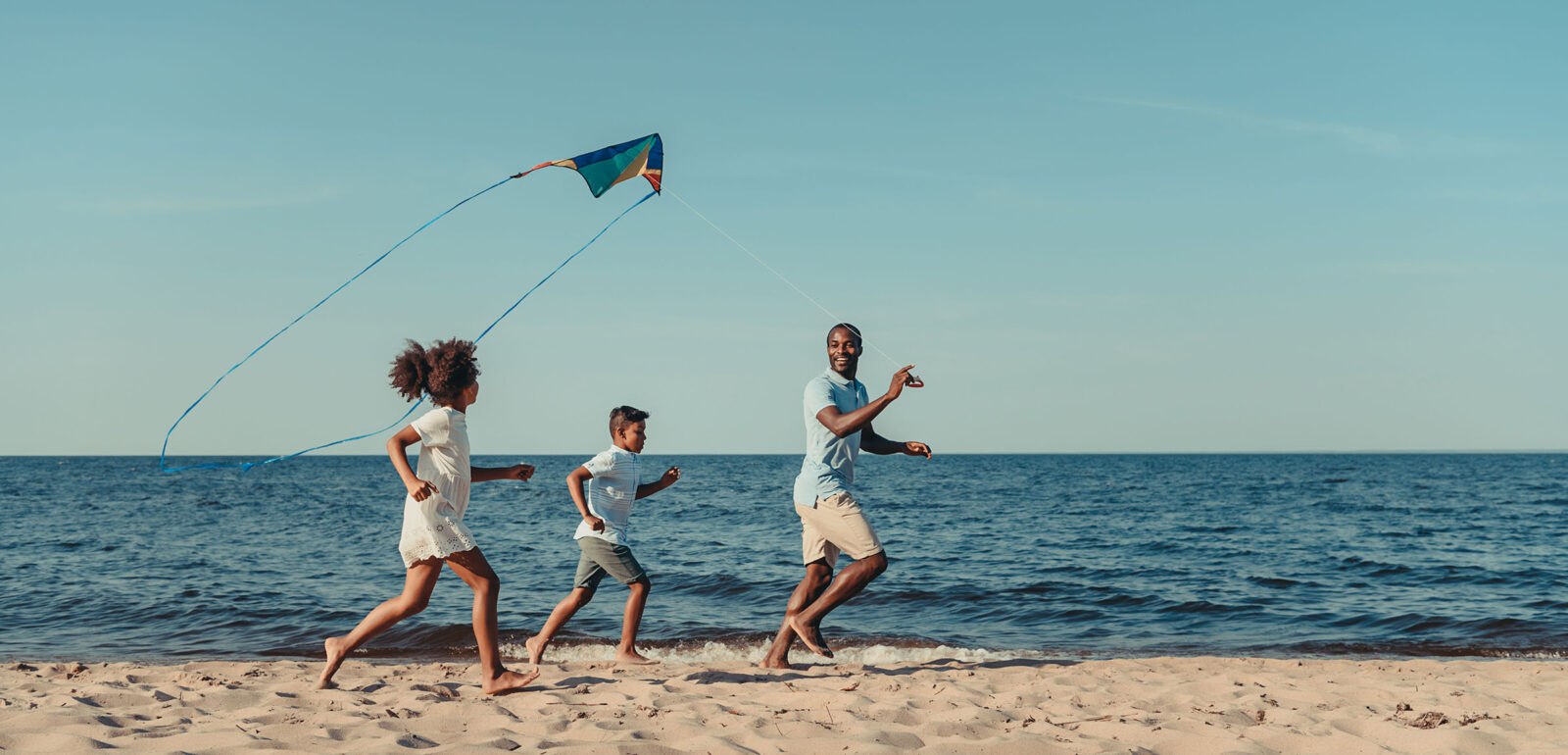 Family running down the beach flying a kite