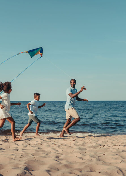 Family running down the beach flying a kite