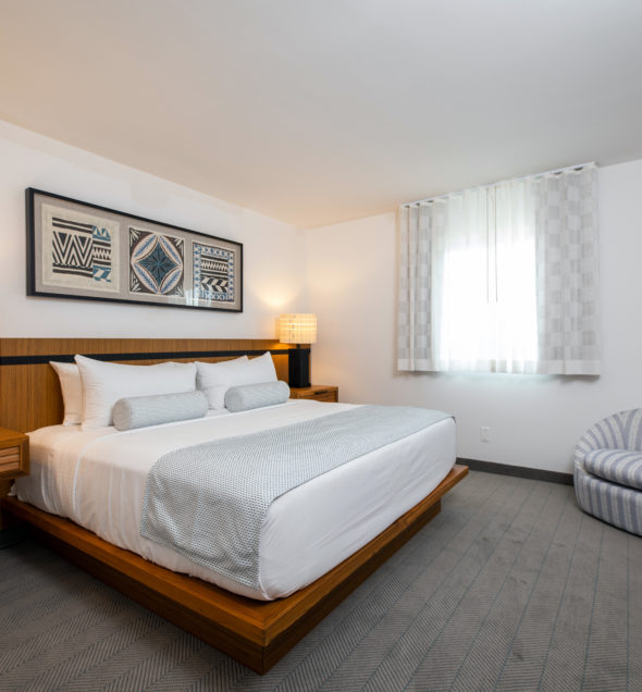 Signature Mahalo Suite with brown wooden platform bed and island artwork at our Diamond Beach hotel
