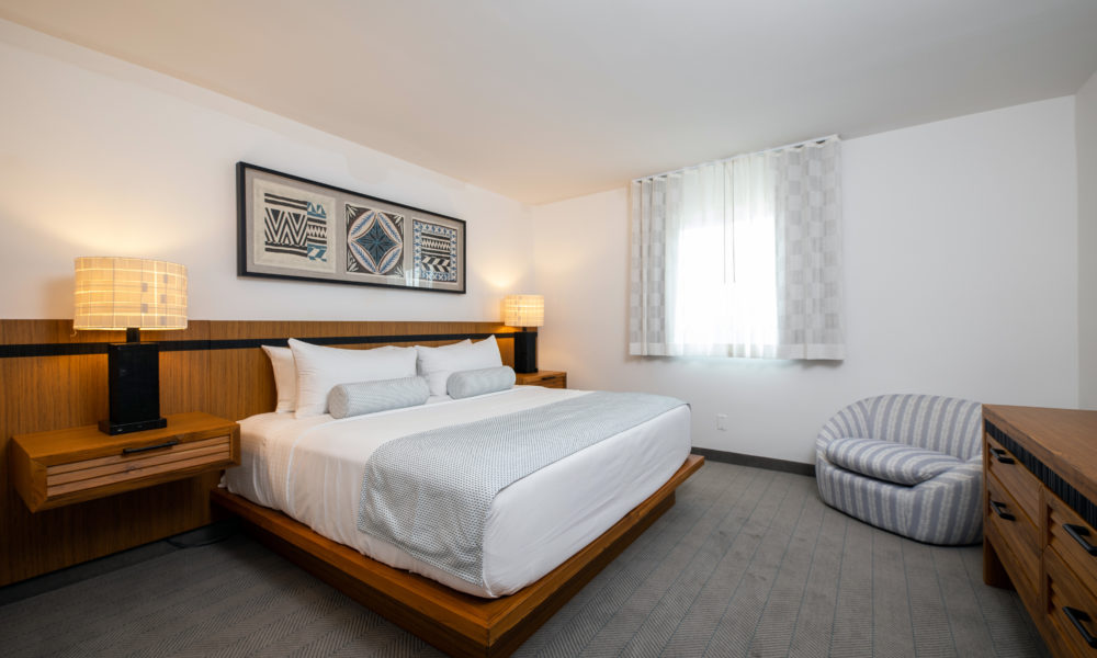Signature Mahalo Suite Bedroom with large brown wooden headboard and platform, plush white bedding, and island artwork
