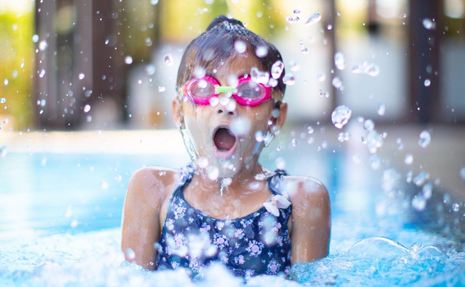 Little girl gasping as she splashes in pool with goggles on